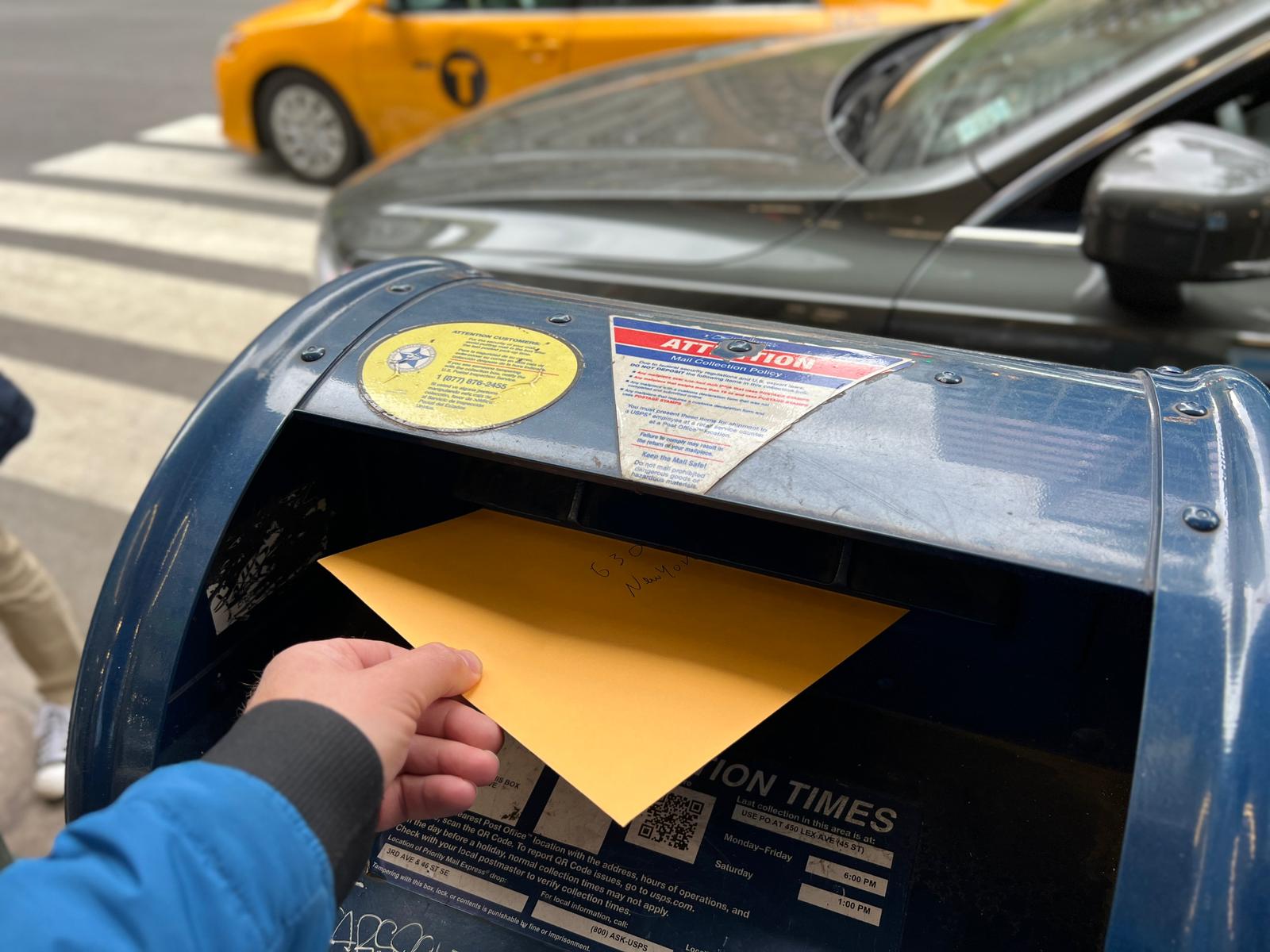 Ein gelber Briefumschlag wird in einen New Yorker Briefkasten eingeworfen.