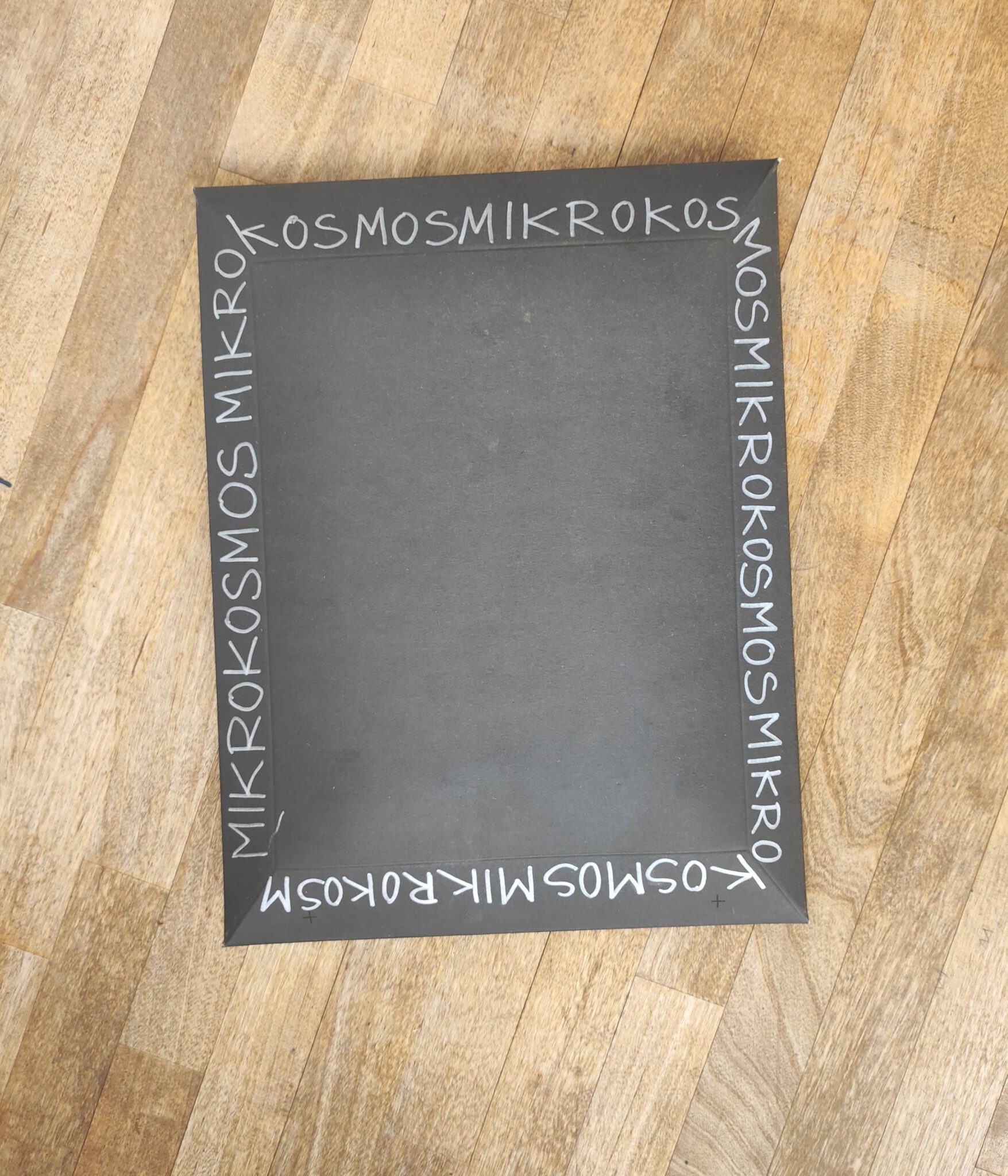 Ein schwarzer Umschkag mit der sich wiederholenden handschriftlichen Aufschrift Mirkokosmos liegt auf einem Holztisch