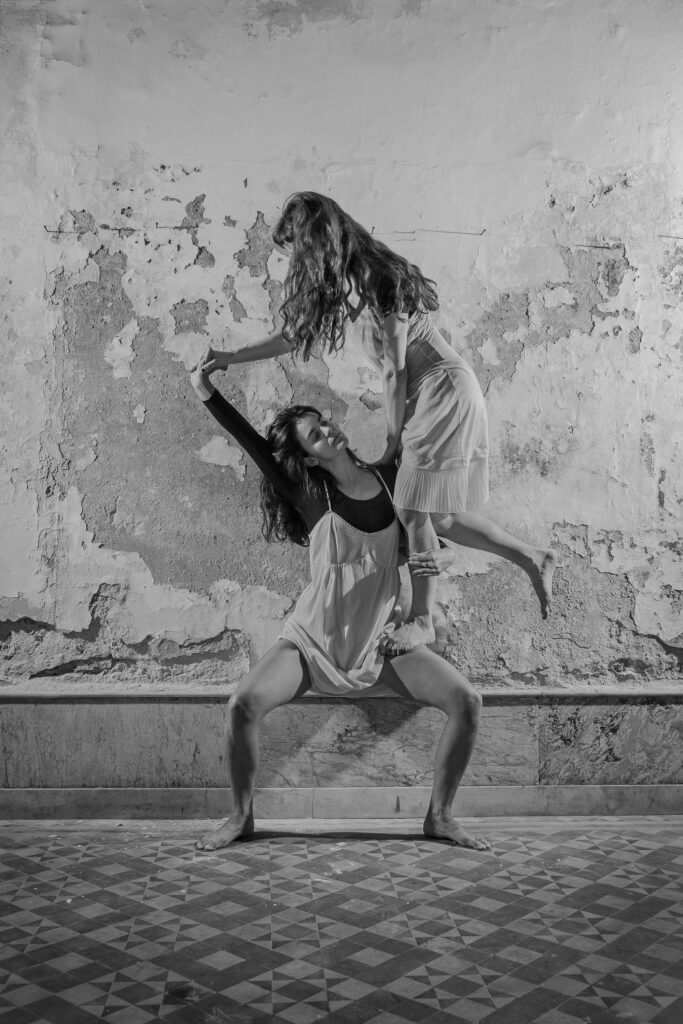 Schwarz/weiss Foto von zwei Tänzerinnen vor einer brökelnden Wand